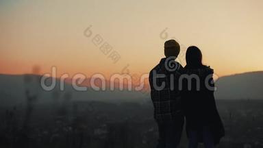 恋爱中的年轻夫妇在山上欣赏日落的剪影。 假期，旅行，浪漫，求婚